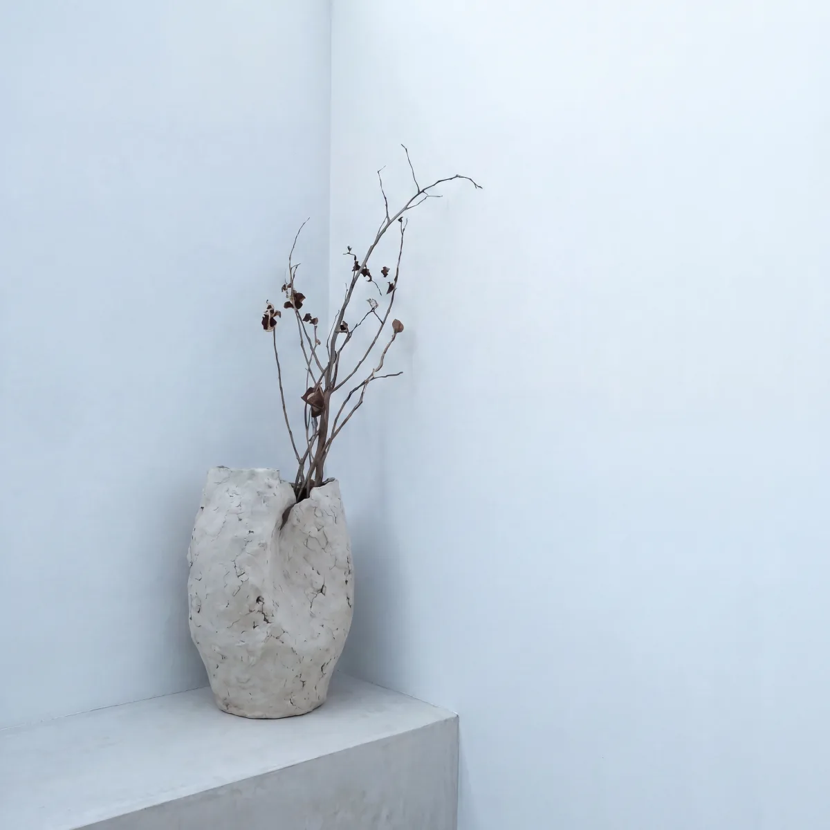 Dried branches in a stone vase on a white pedestal